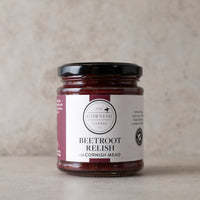 A glass jar of Beetroot Relish made with Cornish Mead by The Cornish Larder, featuring a white label with burgundy accents and a black lid, set against a neutral textured beige background.