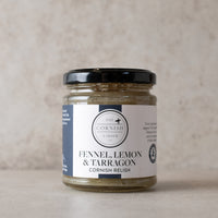 A glass jar of Fennel Relish by The Cornish Larder, featuring a black lid and a white label with navy blue accents, set against a neutral textured beige background.