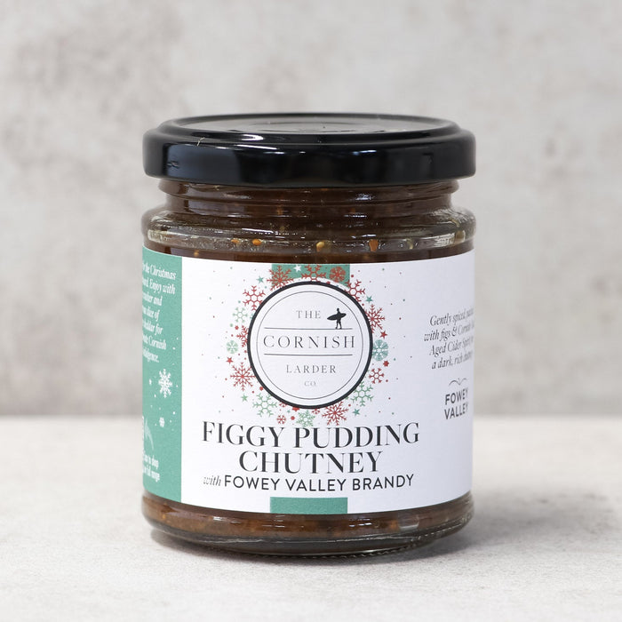 A glass jar of Figgy Pudding Chutney by The Cornish Larder, featuring a black lid and a white label with green and red accents, set against a neutral light grey background.